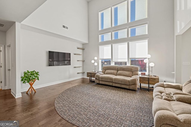 living room with a towering ceiling and dark wood-type flooring