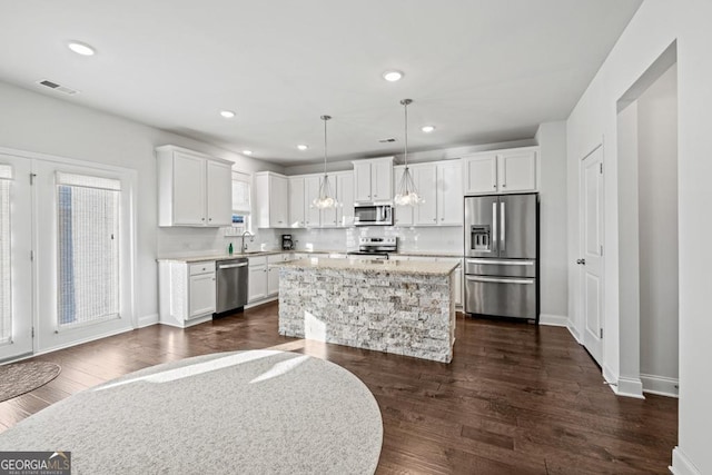 kitchen with stainless steel appliances, a center island, sink, white cabinetry, and decorative light fixtures