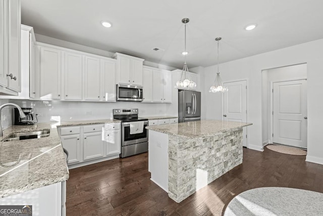 kitchen with stainless steel appliances, sink, decorative light fixtures, white cabinetry, and a center island