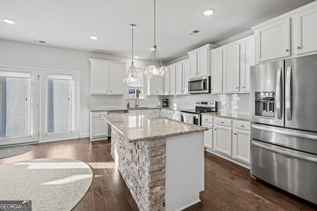 kitchen featuring light stone countertops, a center island, white cabinets, appliances with stainless steel finishes, and sink