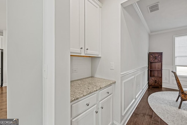 bar with light stone counters, ornamental molding, dark hardwood / wood-style floors, and white cabinetry