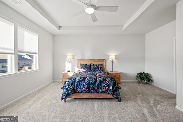 carpeted bedroom with ceiling fan and a tray ceiling