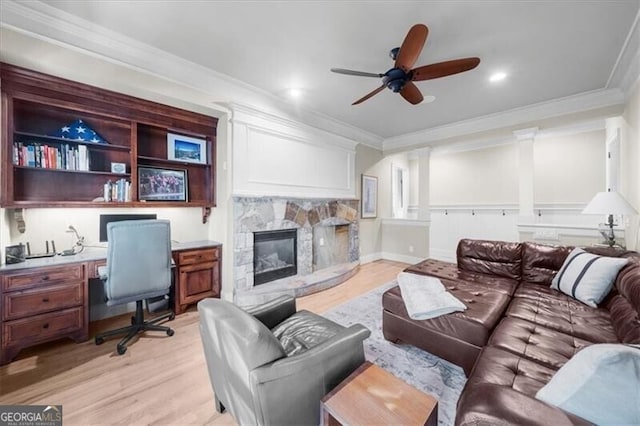 living room featuring built in desk, a fireplace, ceiling fan, ornamental molding, and light hardwood / wood-style floors