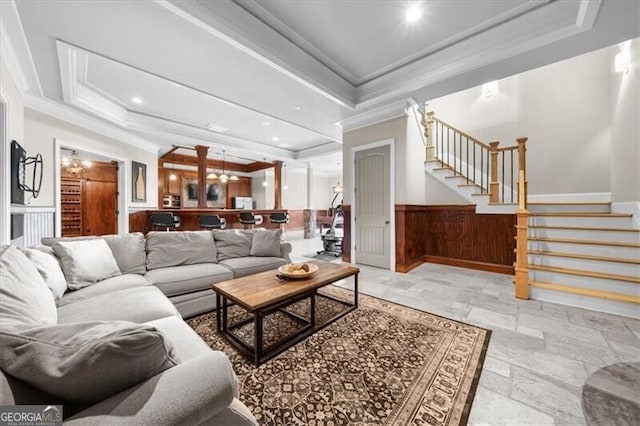 living room with ornamental molding, wood walls, a chandelier, and a tray ceiling