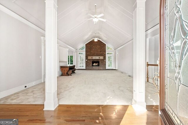 unfurnished living room with ceiling fan, vaulted ceiling, a fireplace, carpet flooring, and ornate columns