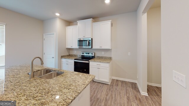 kitchen with light stone counters, stainless steel appliances, light wood-type flooring, white cabinets, and sink