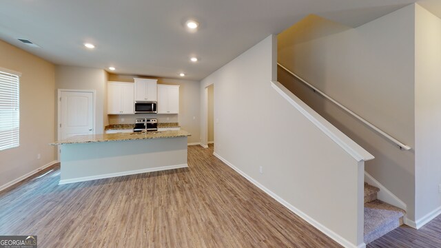 kitchen featuring white cabinetry, stainless steel appliances, an island with sink, light stone counters, and light hardwood / wood-style flooring