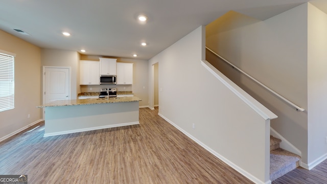 kitchen with light stone counters, a kitchen island with sink, stainless steel appliances, visible vents, and white cabinetry