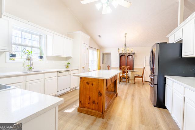 kitchen featuring sink, white cabinetry, dishwasher, vaulted ceiling, and a kitchen island