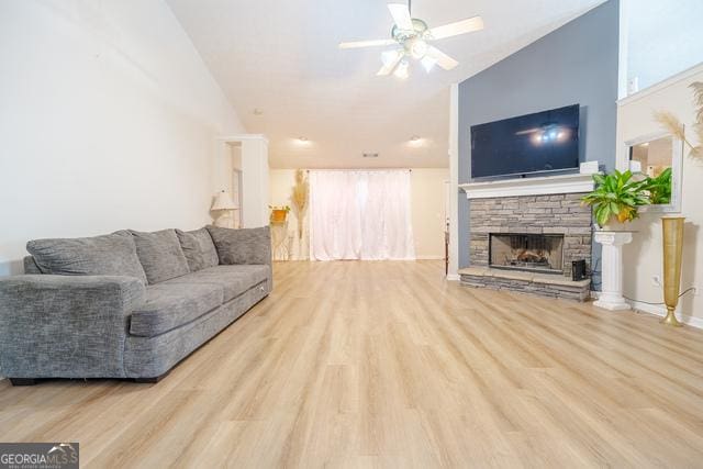 living room with lofted ceiling, ceiling fan, light hardwood / wood-style flooring, and a stone fireplace