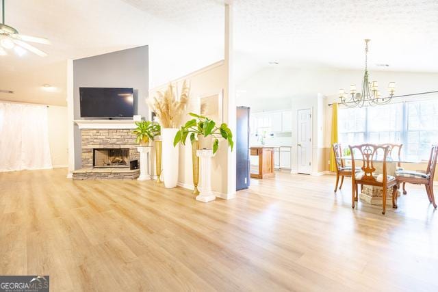 living room with light wood-type flooring, a stone fireplace, vaulted ceiling, and ceiling fan with notable chandelier