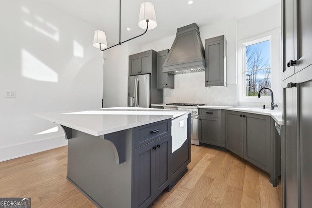 kitchen featuring stainless steel appliances, sink, hanging light fixtures, premium range hood, and a kitchen island