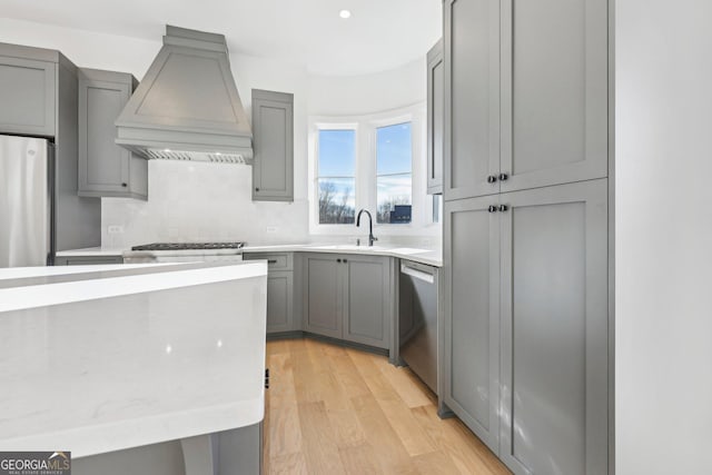 kitchen featuring sink, light hardwood / wood-style floors, custom exhaust hood, gray cabinetry, and appliances with stainless steel finishes