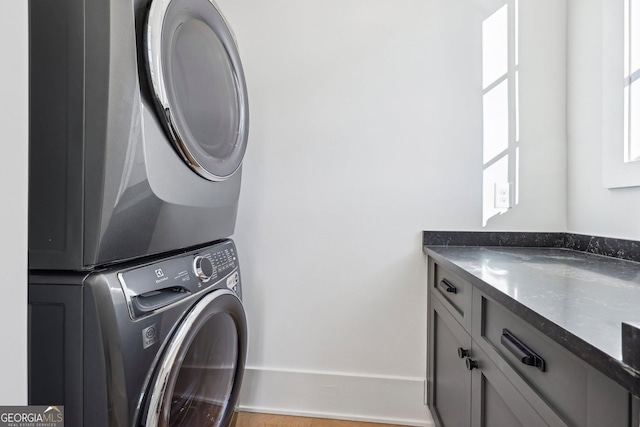 washroom featuring stacked washer and dryer and cabinets