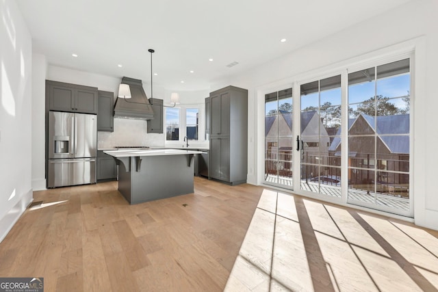 kitchen with a breakfast bar area, light hardwood / wood-style floors, hanging light fixtures, stainless steel appliances, and premium range hood