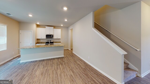 kitchen featuring a kitchen island with sink, appliances with stainless steel finishes, light stone counters, white cabinets, and light hardwood / wood-style flooring