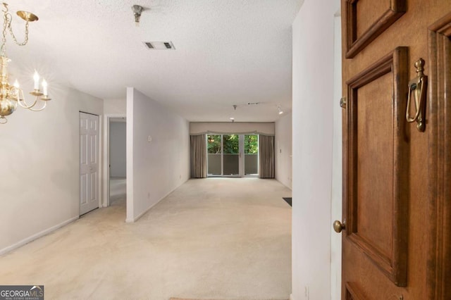 corridor featuring light colored carpet, rail lighting, a textured ceiling, and a chandelier