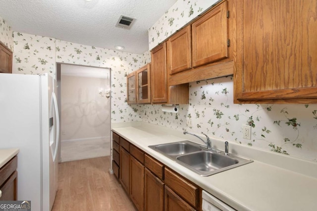 kitchen featuring white refrigerator with ice dispenser, a textured ceiling, light hardwood / wood-style floors, and sink