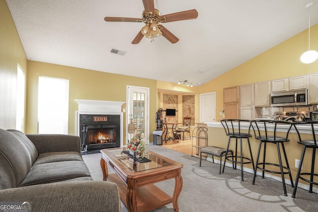 living room with light carpet, visible vents, a ceiling fan, vaulted ceiling, and a lit fireplace