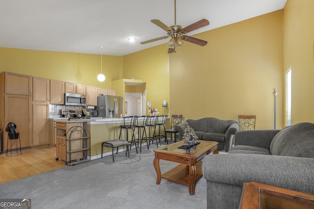 living area featuring high vaulted ceiling, light carpet, and a ceiling fan