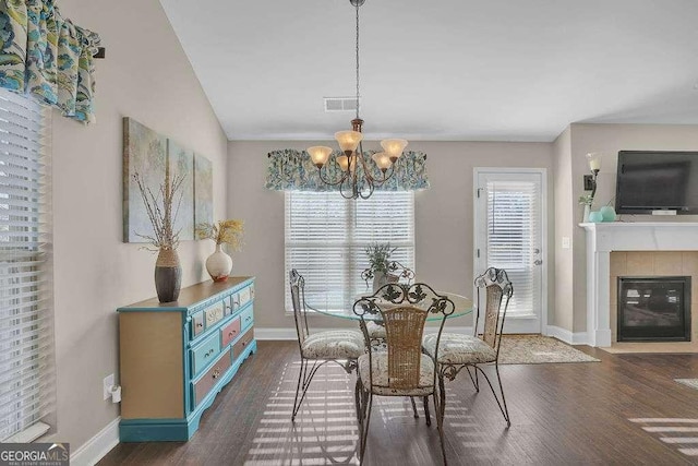 dining room featuring lofted ceiling, a tiled fireplace, a chandelier, and dark hardwood / wood-style floors