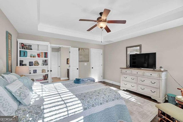 bedroom with wood-type flooring, ceiling fan, a tray ceiling, and ornamental molding