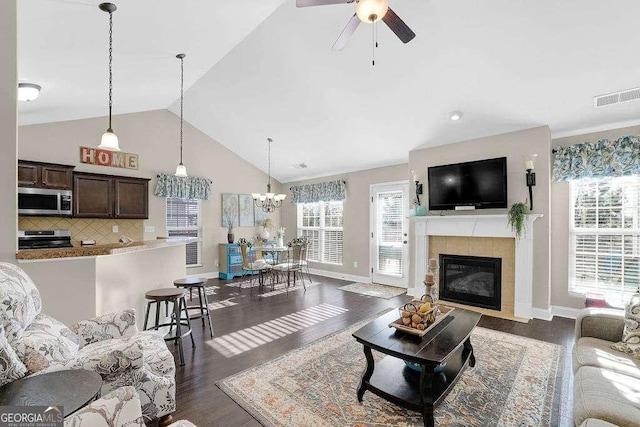 living room with ceiling fan with notable chandelier, dark hardwood / wood-style flooring, a tile fireplace, and lofted ceiling