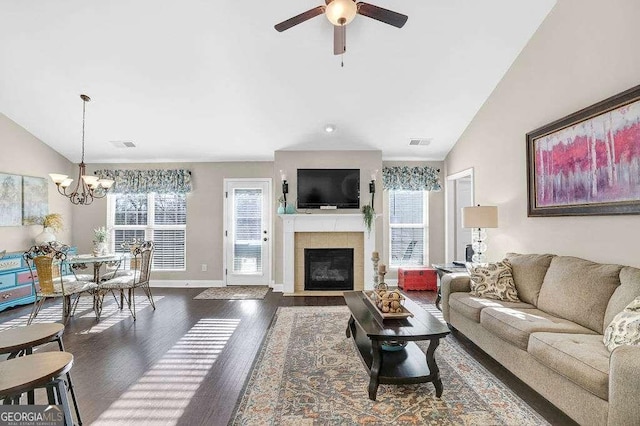 living room featuring ceiling fan with notable chandelier, a tiled fireplace, vaulted ceiling, and dark hardwood / wood-style flooring