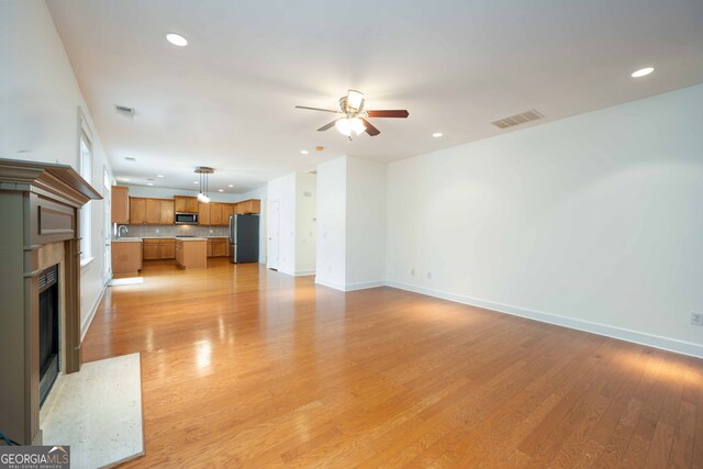 unfurnished living room with ceiling fan, light hardwood / wood-style flooring, and sink