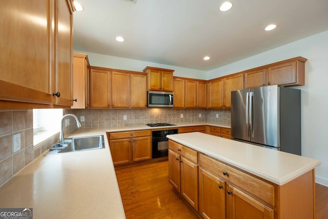 kitchen with appliances with stainless steel finishes, a center island, decorative backsplash, hardwood / wood-style flooring, and sink