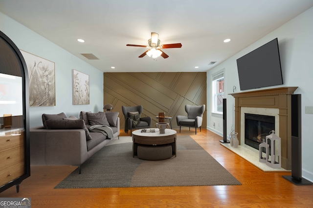 living room with a high end fireplace, ceiling fan, and light hardwood / wood-style floors