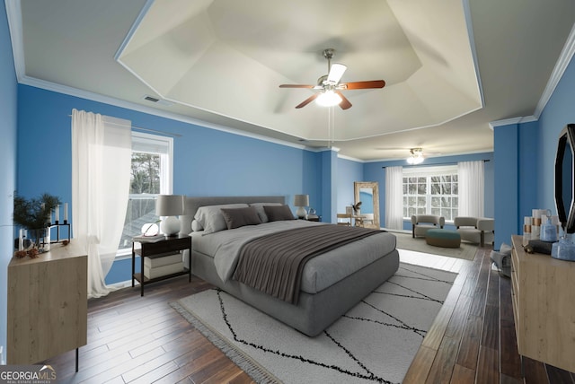 bedroom with ceiling fan, a tray ceiling, ornamental molding, and dark hardwood / wood-style floors