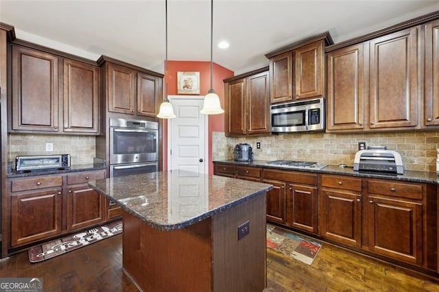 kitchen with stainless steel appliances, hanging light fixtures, a center island, dark stone counters, and dark wood-type flooring