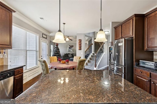 kitchen featuring stainless steel appliances, decorative light fixtures, ornamental molding, and dark stone counters