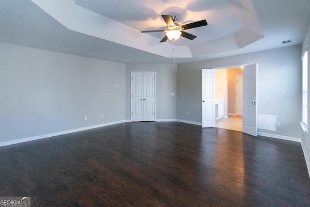 empty room featuring ceiling fan, a tray ceiling, and dark hardwood / wood-style flooring