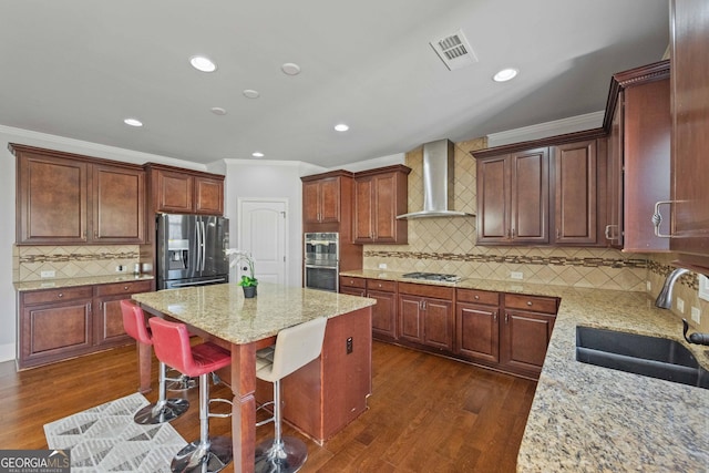 kitchen featuring a center island, sink, light stone countertops, appliances with stainless steel finishes, and wall chimney exhaust hood