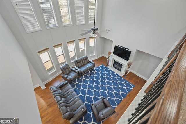 living room with dark wood-type flooring, ceiling fan, and a high ceiling