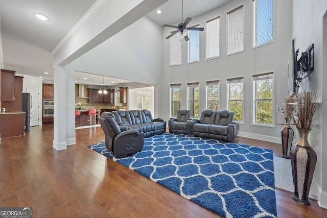 living room with ceiling fan, dark wood-type flooring, a high ceiling, and ornamental molding