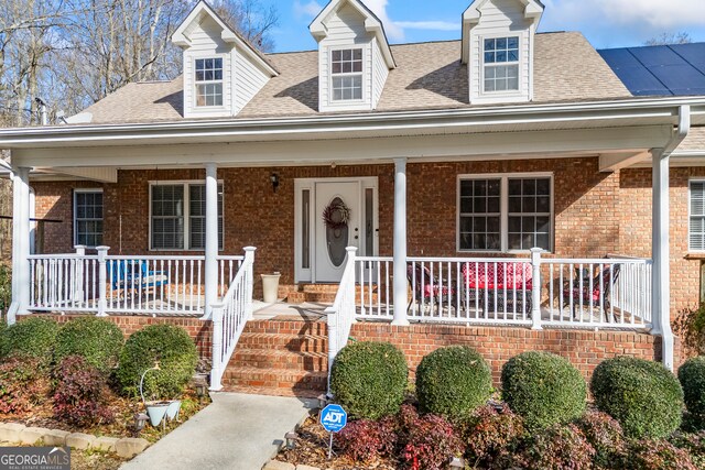 new england style home featuring a front yard, a porch, and solar panels