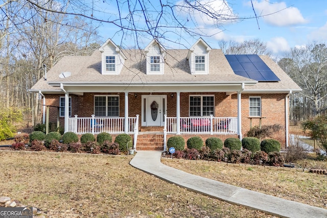 cape cod-style house featuring a porch, a front lawn, and solar panels