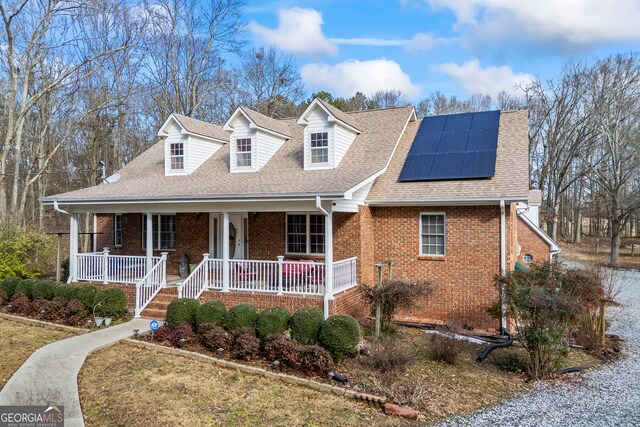 cape cod home featuring solar panels and covered porch