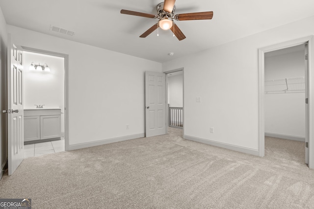 unfurnished bedroom featuring a spacious closet, ceiling fan, a closet, ensuite bath, and light colored carpet