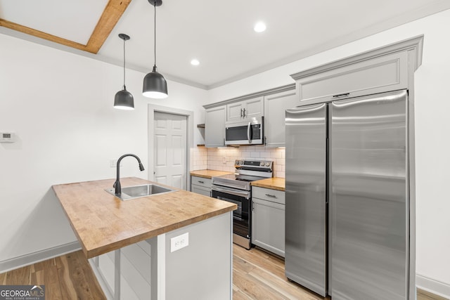 kitchen with pendant lighting, stainless steel appliances, wood counters, gray cabinetry, and sink