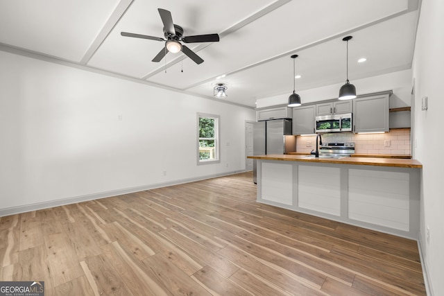 kitchen with appliances with stainless steel finishes, gray cabinetry, hanging light fixtures, wood counters, and decorative backsplash