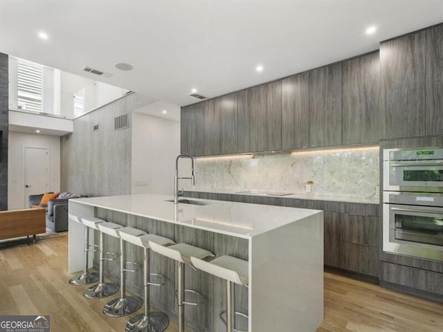 kitchen featuring sink, a breakfast bar, an island with sink, and stainless steel double oven