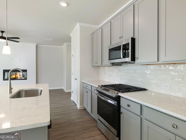 kitchen featuring a large fireplace, stainless steel appliances, crown molding, gray cabinetry, and a sink