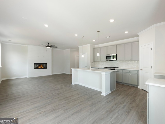 kitchen featuring stainless steel microwave, gray cabinetry, light wood-style floors, a fireplace, and backsplash