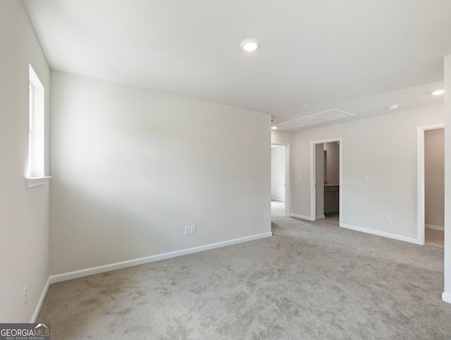 carpeted empty room featuring attic access and baseboards