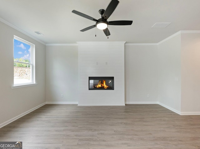 unfurnished living room with a fireplace, visible vents, wood finished floors, and ornamental molding