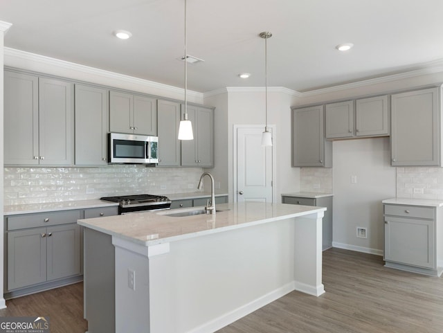 kitchen with stainless steel microwave, gray cabinetry, a sink, wood finished floors, and gas range